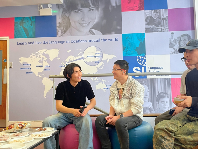 Two students chatting and enjoying the Chuseok (Korean Mid-Autumn Festival) celebration at LSI London, surrounded by fellow students and a festive atmosphere during the cultural event held at the language school.