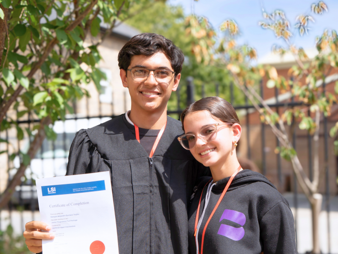Two students from the LSI Summer Junior Programme in Cambridge standing outdoors on a sunny day after completing their English language course. One student is proudly holding an LSI certificate following their graduation, celebrating their achievement and progress in English language learning. The image highlights the international student experience offered by LSI Junior Programmes, combining English lessons, cultural immersion, international friendships, and personal development in one of the UK's most popular study destinations for young learners.